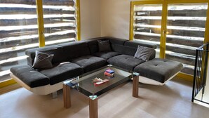 En moderne stue med en modulsofa, et glasbord og store vinduer med trærammer.