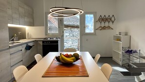 Et moderne køkken med spiseplads, med en central ø med skålvase og frugt, hvide skabe og et hængende lysarmatur.