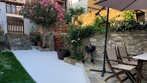 A patio area with a stone wall, a wooden table, and chairs. There is a grill and potted plants. - Beautiful Petrino 1880 (Agios Nikolaos)