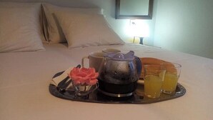 A neatly made bed with white linens, a tray with a teapot, cups, and glasses of orange juice. - Beautiful Petrino 1880 (Agios Nikolaos)