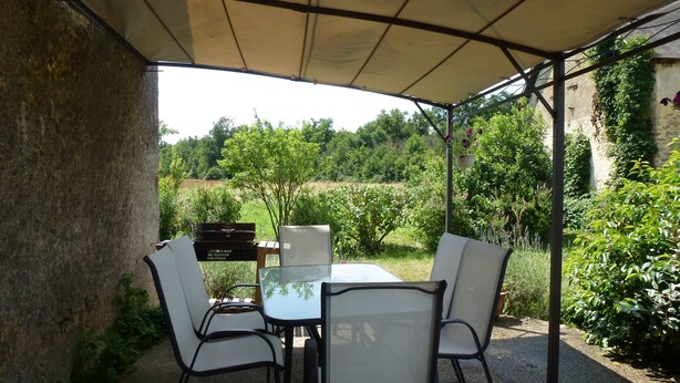 Une terrasse extérieure avec une table et des chaises, un barbecue et une vue sur un jardin et des arbres.