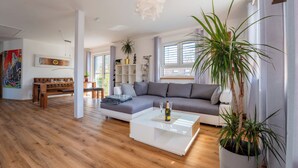 A modern living room with a sectional sofa, a white coffee table, and a large potted plant. - Dießen, Ammersee-Nest, new, bright, 90sqm, 2 bedrooms, balcony, parking spaces, premium (Dießen am Ammersee)