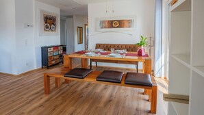 A dining area with a wooden table set for four, a bench with cushions, and a sofa. - Dießen, Ammersee-Nest, new, bright, 90sqm, 2 bedrooms, balcony, parking spaces, premium (Dießen am Ammersee)