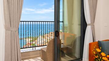 Un balcon avec vue sur la mer, une chaise en osier et un canapé agrémenté d’un vase de fleurs.