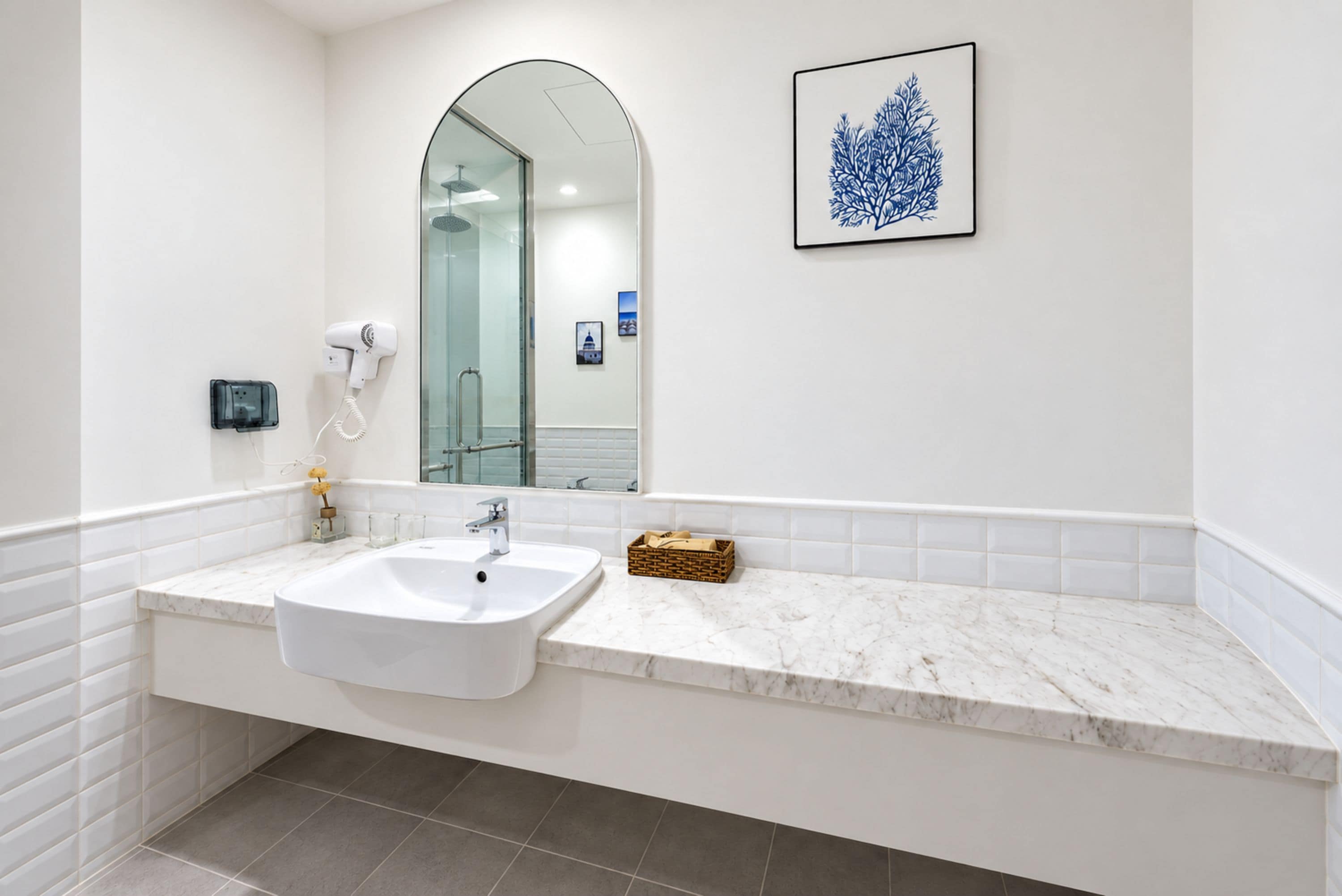 Un baño moderno con un lavamanos blanco, cabina de ducha con mampara de vidrio y una obra de arte enmarcada en la pared.