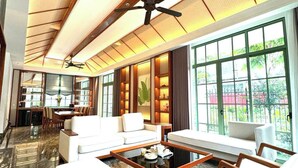 Amplia sala de estar con techo alto, ventilador de techo, zona de comedor con mesa y sillas, y ventanas grandes que ofrecen vistas al exterior.