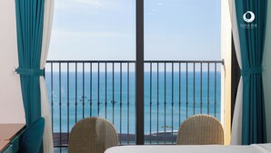 Habitación de hotel con balcón que da al mar, con sillas de mimbre y una cama.