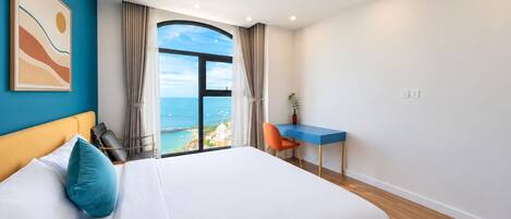 A hotel room with a large bed, a desk, and a view of the sea.