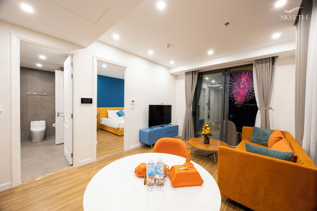 A modern hotel room with a bed, a sofa, a TV, and a dining area.