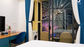 Una camera d'albergo con un letto, una scrivania con una sedia, una lavatrice e vista sui fuochi d'artificio.