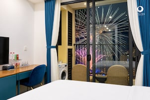 Habitación de hotel con cama, escritorio con silla, lavadora y vista a fuegos artificiales.