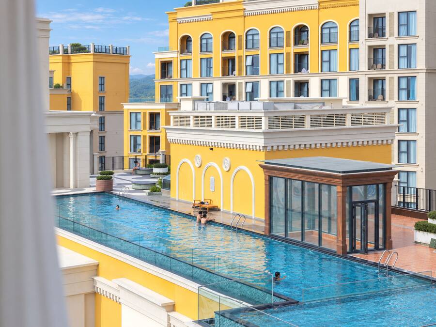 A swimming pool with a glass enclosure, surrounded by yellow buildings with multiple balconies.