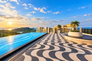 A rooftop infinity pool with a patterned floor, overlooking a coastal landscape with buildings and palm trees.