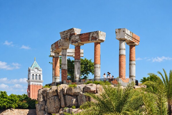 Ruinas antiguas con columnas y una torre del reloj al fondo.