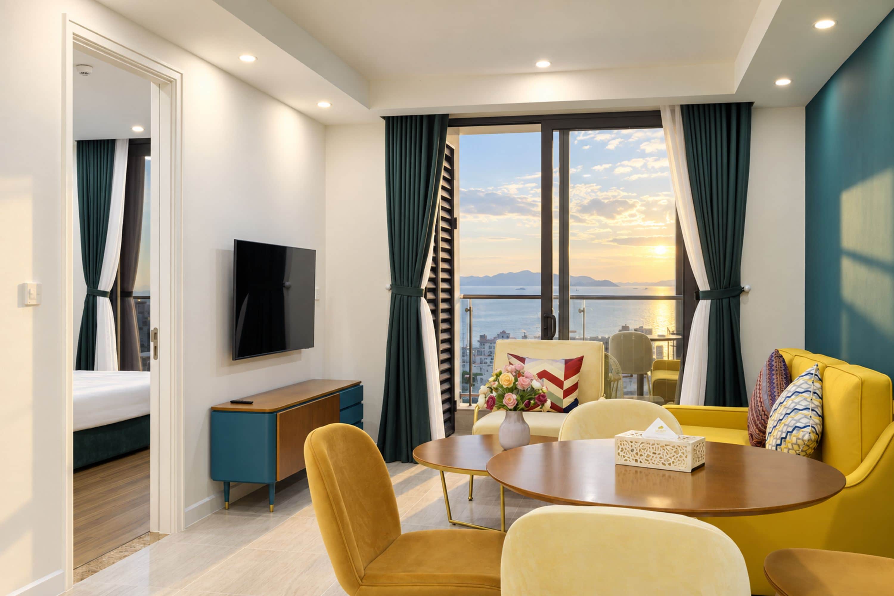 A modern hotel room with a balcony, a dining area, and a TV.