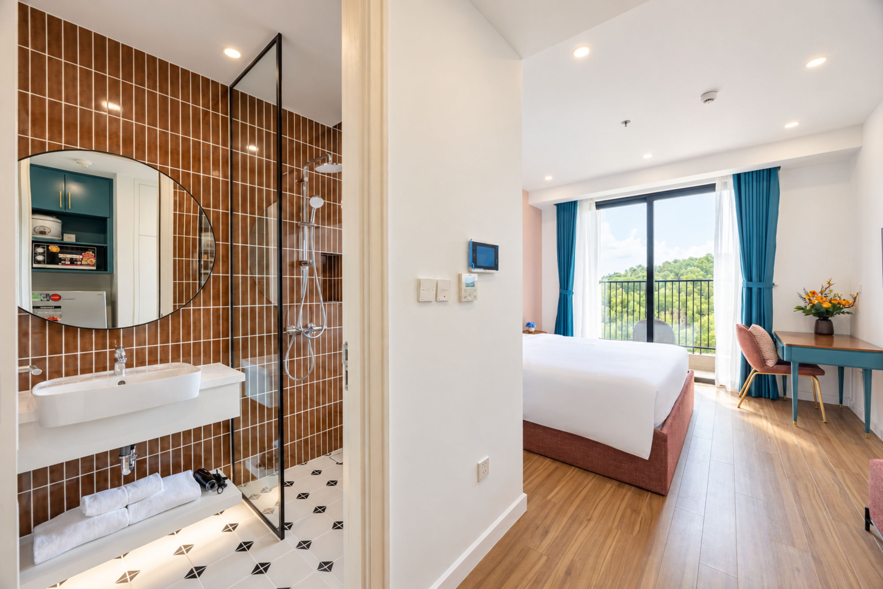 A hotel room with a bathroom, a bed, a desk, and a balcony with a view.