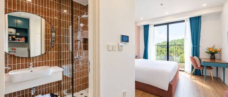 A hotel room with a bathroom, a bed, a desk, and a balcony with a view.