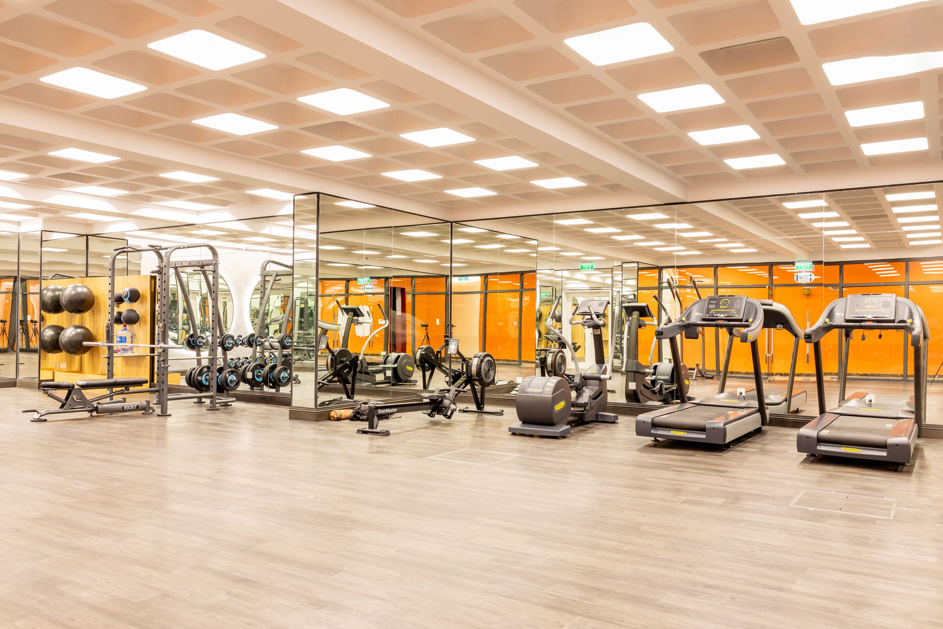 A gym with various exercise equipment, mirrored walls, and a wooden floor.