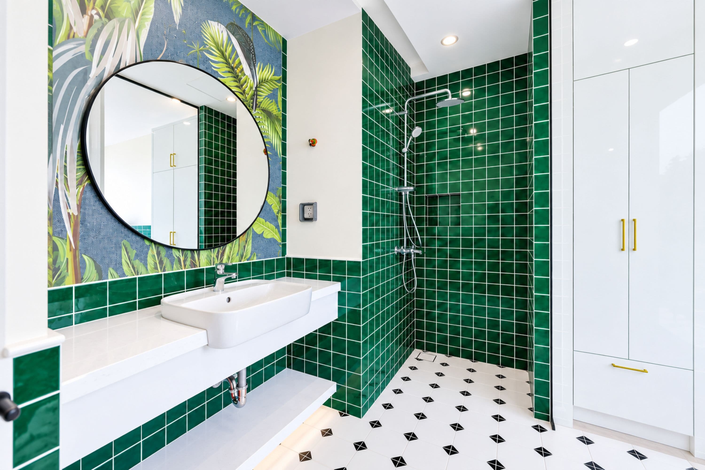 A bathroom with a white sink, a mirror, green tiles, a shower, and a white cabinet.