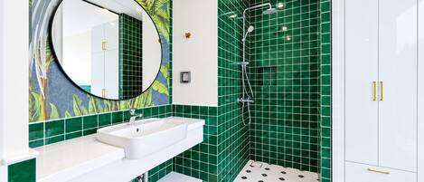 A bathroom with a white sink, a mirror, green tiles, a shower, and a white cabinet.