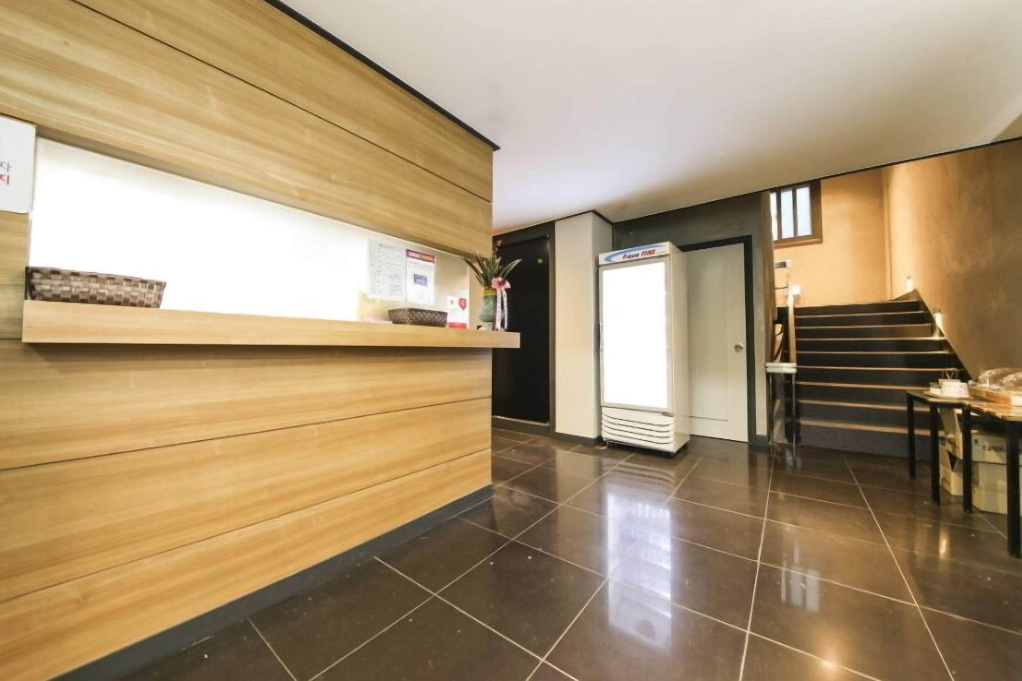 A reception area with a wooden reception desk, a refrigerator, and a staircase leading to another floor.