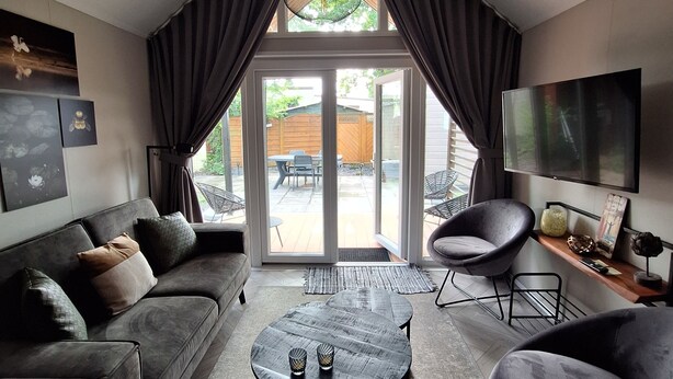 A modern living room with a grey sofa, a round coffee table, and a TV on the wall. - Tinyhouse / chalet at the Rhederlaagse Meren vacation park in NL-Lathum by the lake (Lathum)