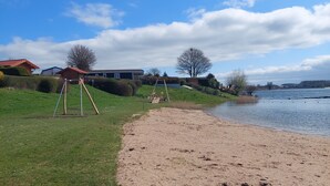 A sandy beach with a grassy area and a swing set. There are houses in the background. - Tinyhouse / chalet at the Rhederlaagse Meren vacation park in NL-Lathum by the lake (Lathum)