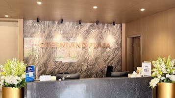 A reception desk with a marble wall, a sign reading 'GREENLAND PLAZA', and a HP computer.