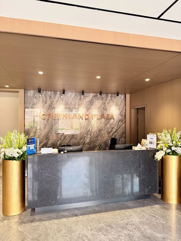 A reception desk with a marble wall, a sign reading 'GREENLAND PLAZA', and a HP computer. - Greenland Apartment by Link (Kigali)