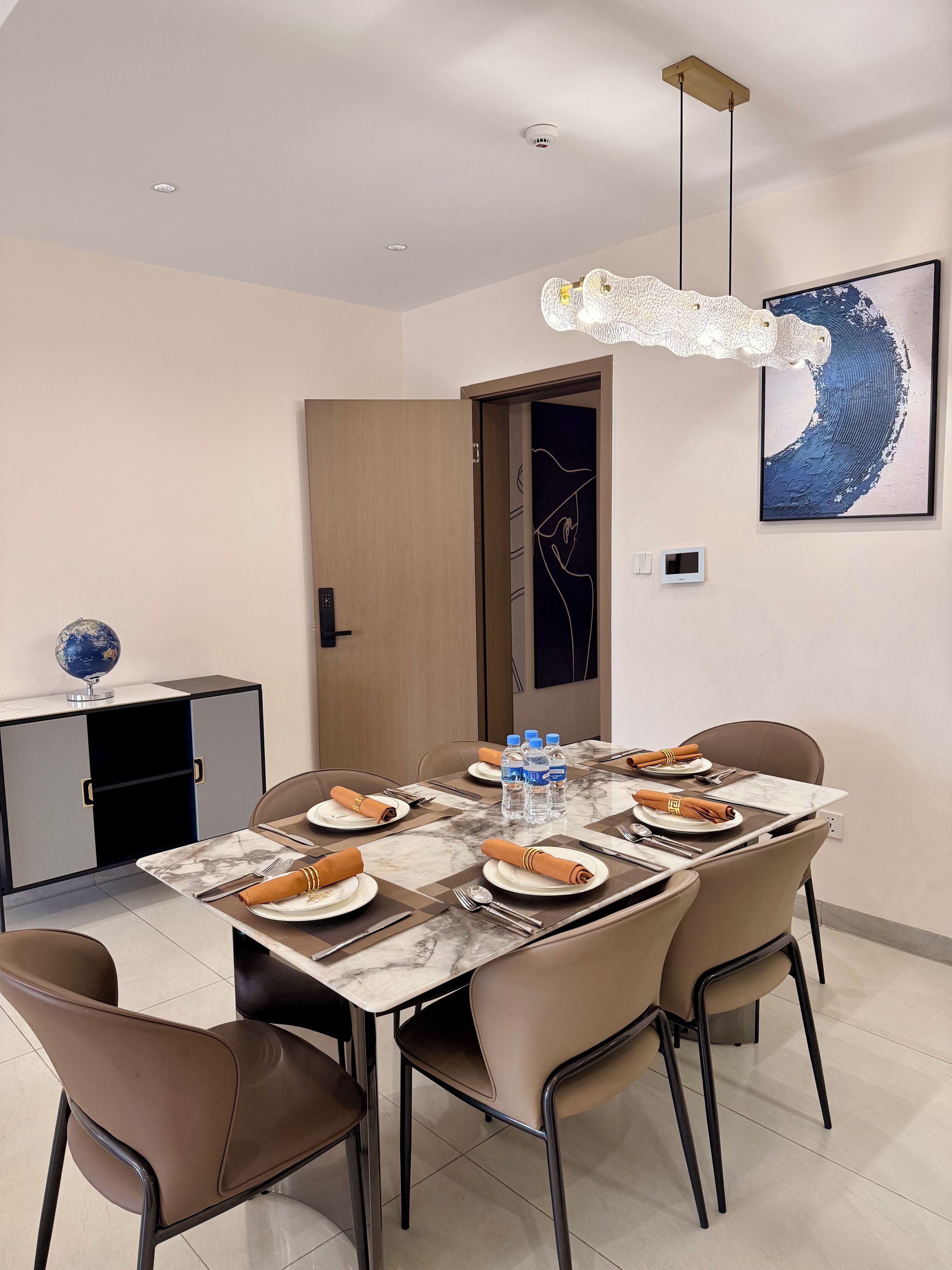 Un comedor con una mesa de mármol dispuesta para cuatro personas, equipada con botellas de agua, platos y cubiertos.