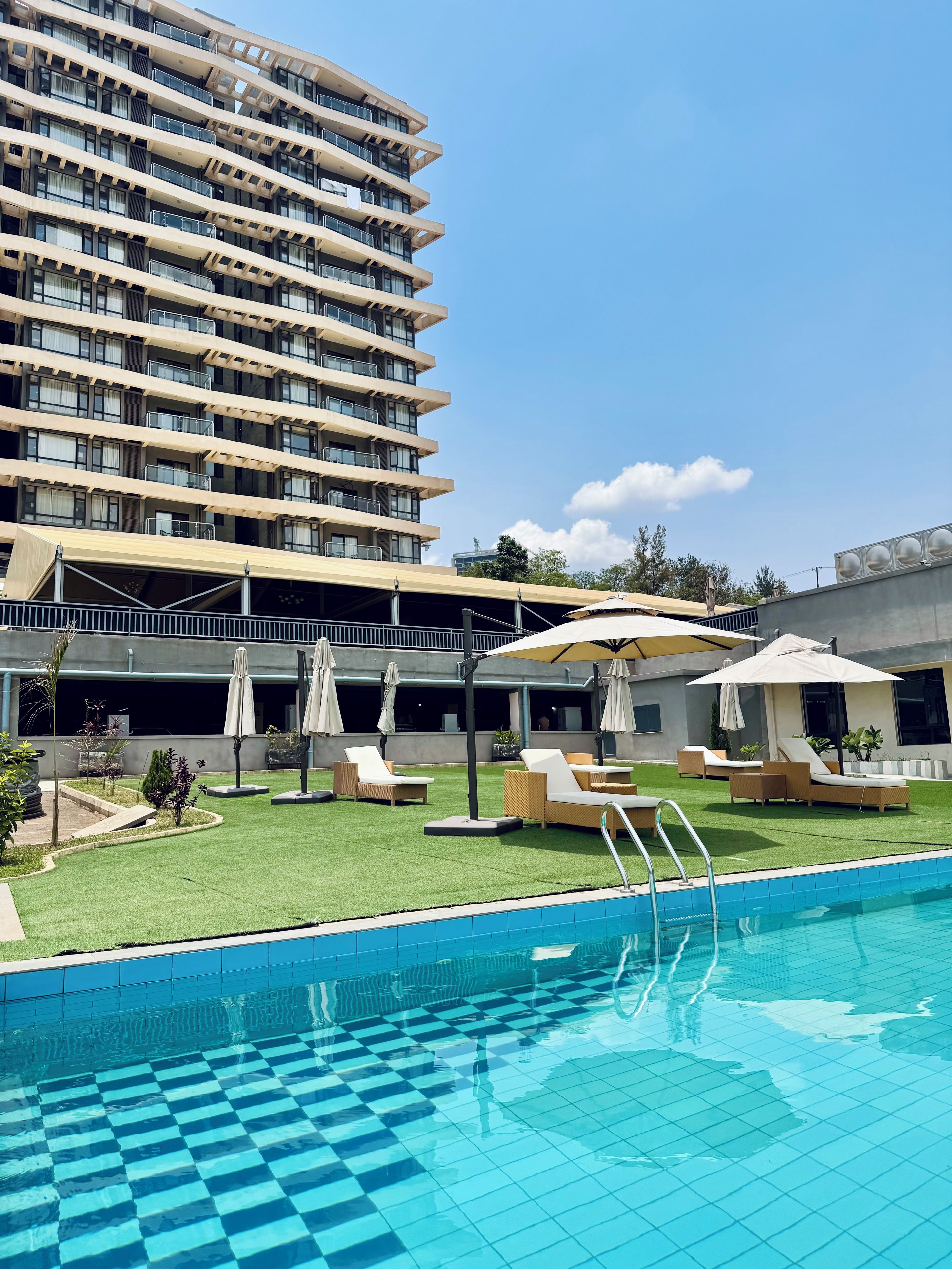 Un hotel con piscina, zona de estar al aire libre y un edificio alto al fondo.