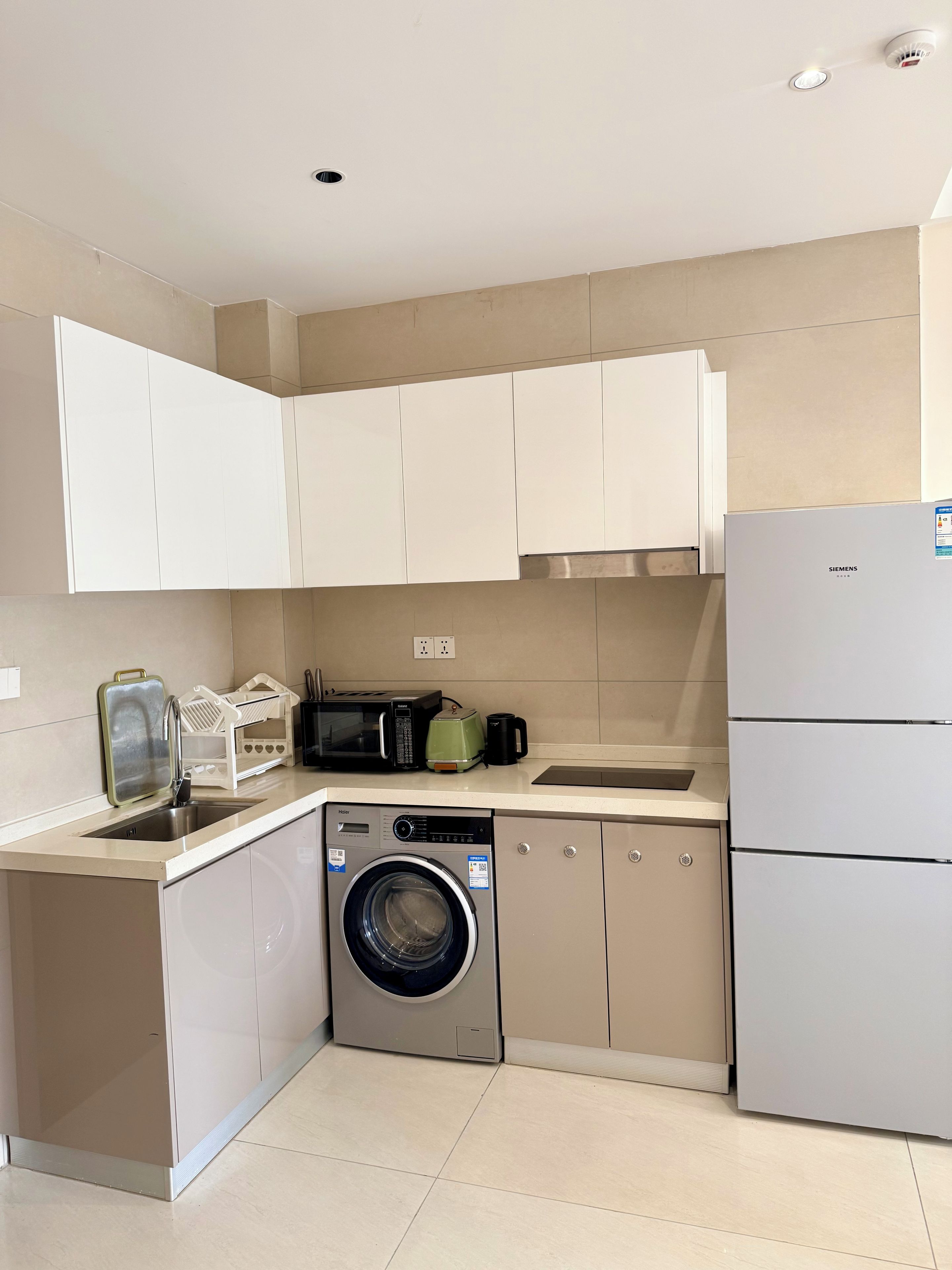 Una cocina compacta equipada con lavadora, microondas, hervidor y refrigerador.