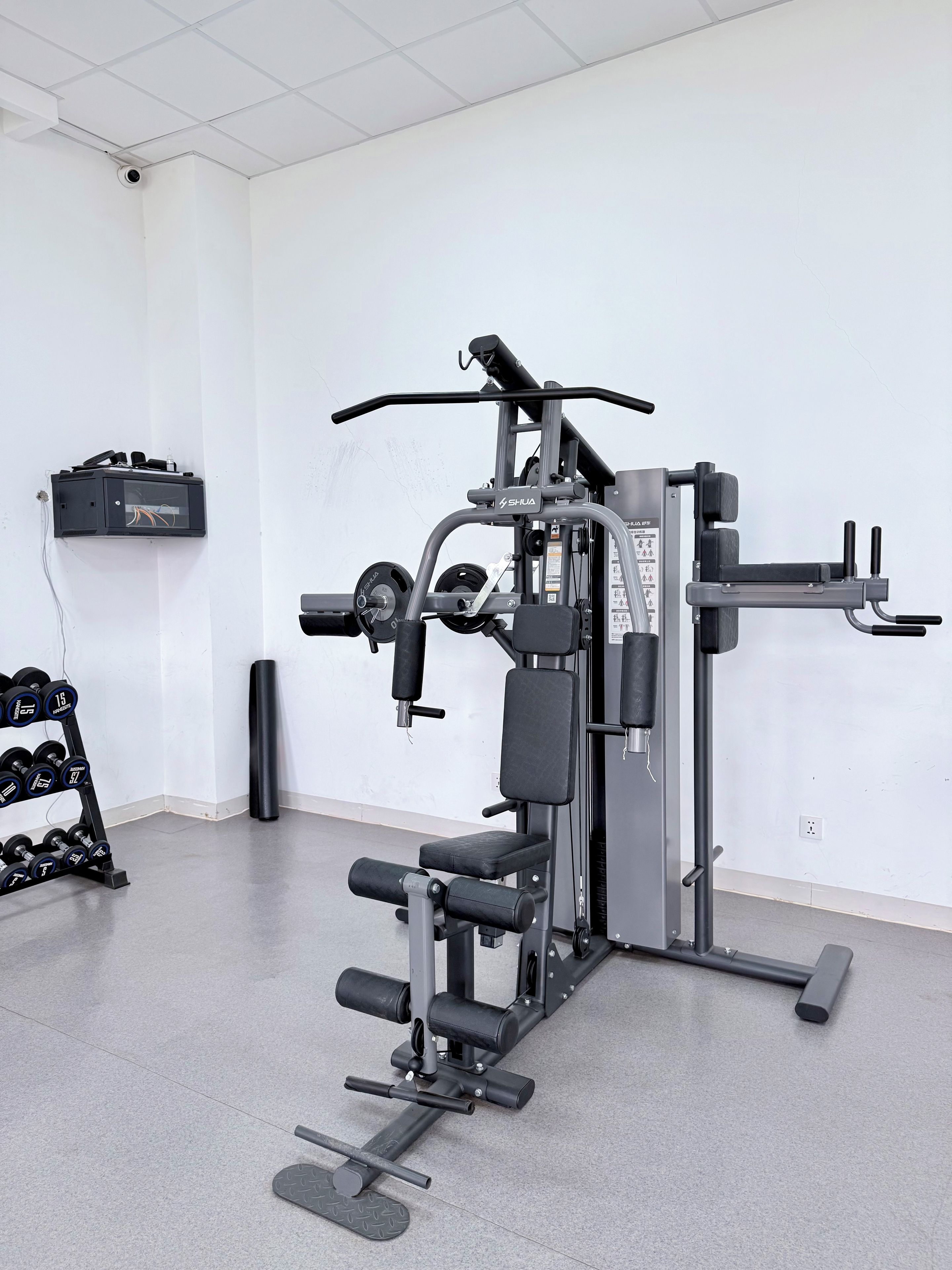 A gym with various exercise equipment, a wall-mounted electrical box, and a rack of dumbbells.