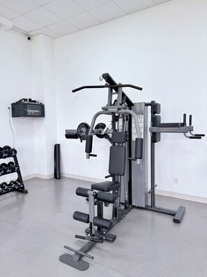 Un gimnasio con equipos de ejercicio variados, un cuadro eléctrico en la pared y un estante con mancuernas.