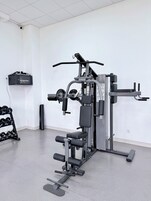 Un gimnasio con equipos de ejercicio variados, un cuadro eléctrico en la pared y un estante con mancuernas.