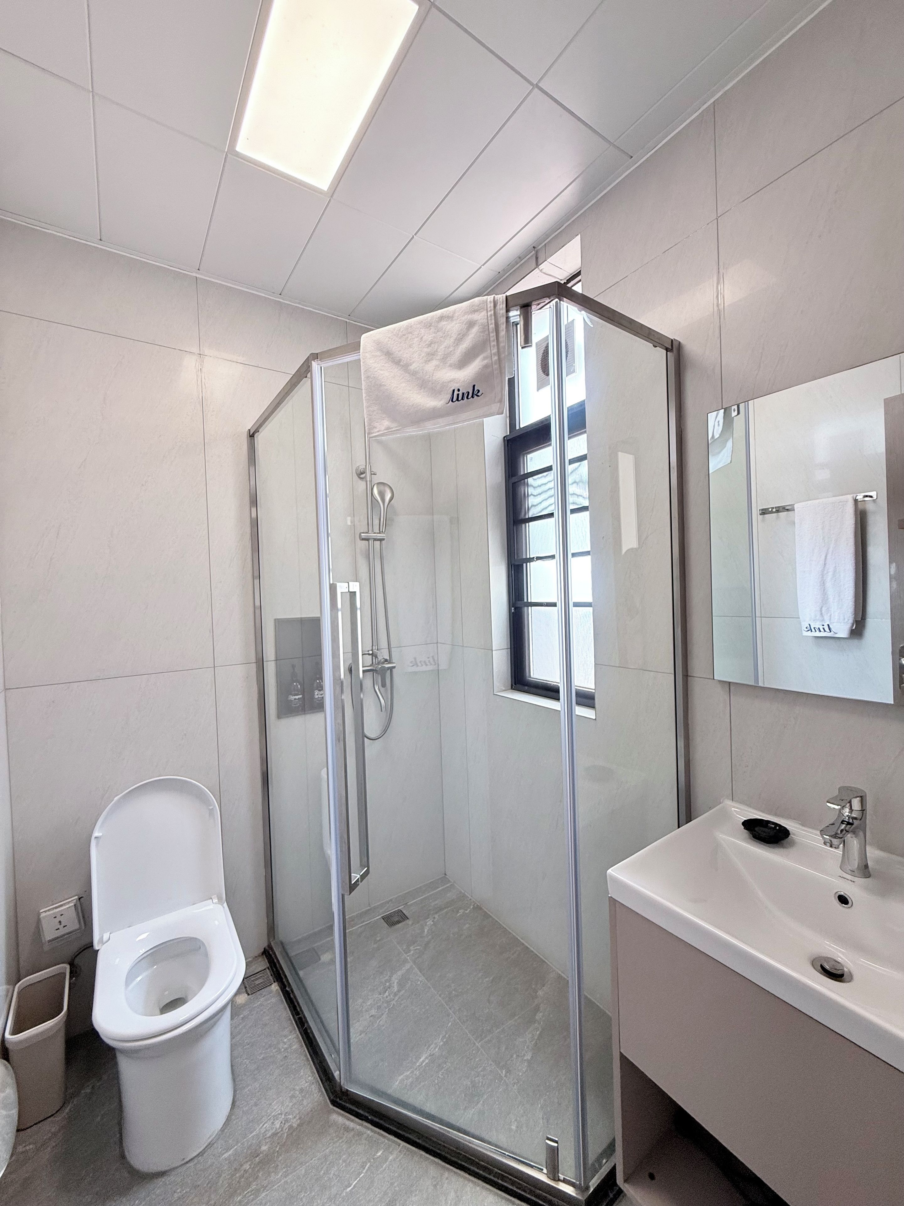 Un baño moderno con ducha envuelta en vidrio, inodoro blanco y lavamanos con espejo.
