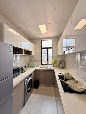 A compact kitchen with a built-in washing machine, a sink, and a stove. - Greenland Apartment by Link (Kigali)
