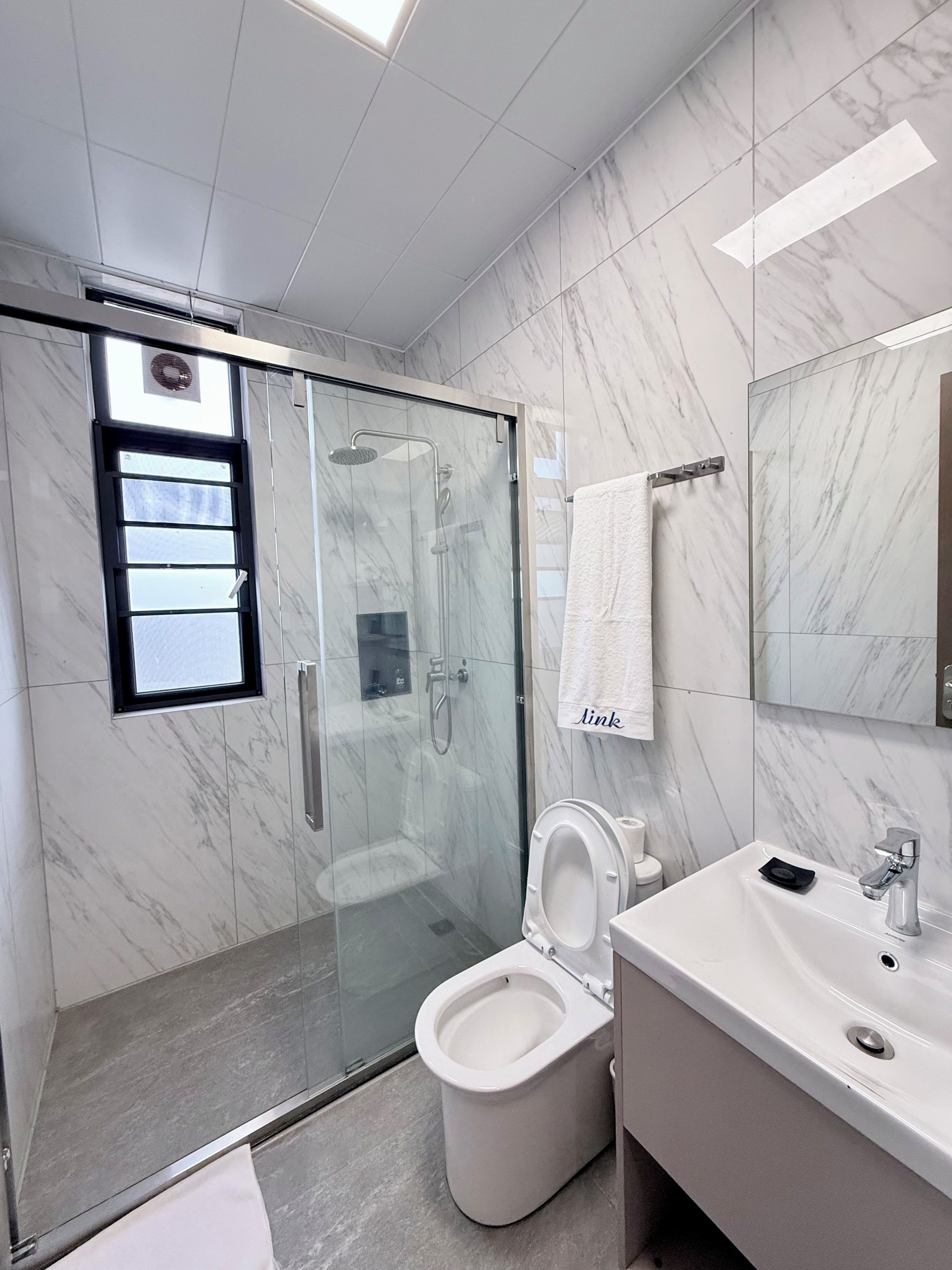 A modern bathroom with a glass-enclosed shower, a toilet, and a sink with a mirror above it.