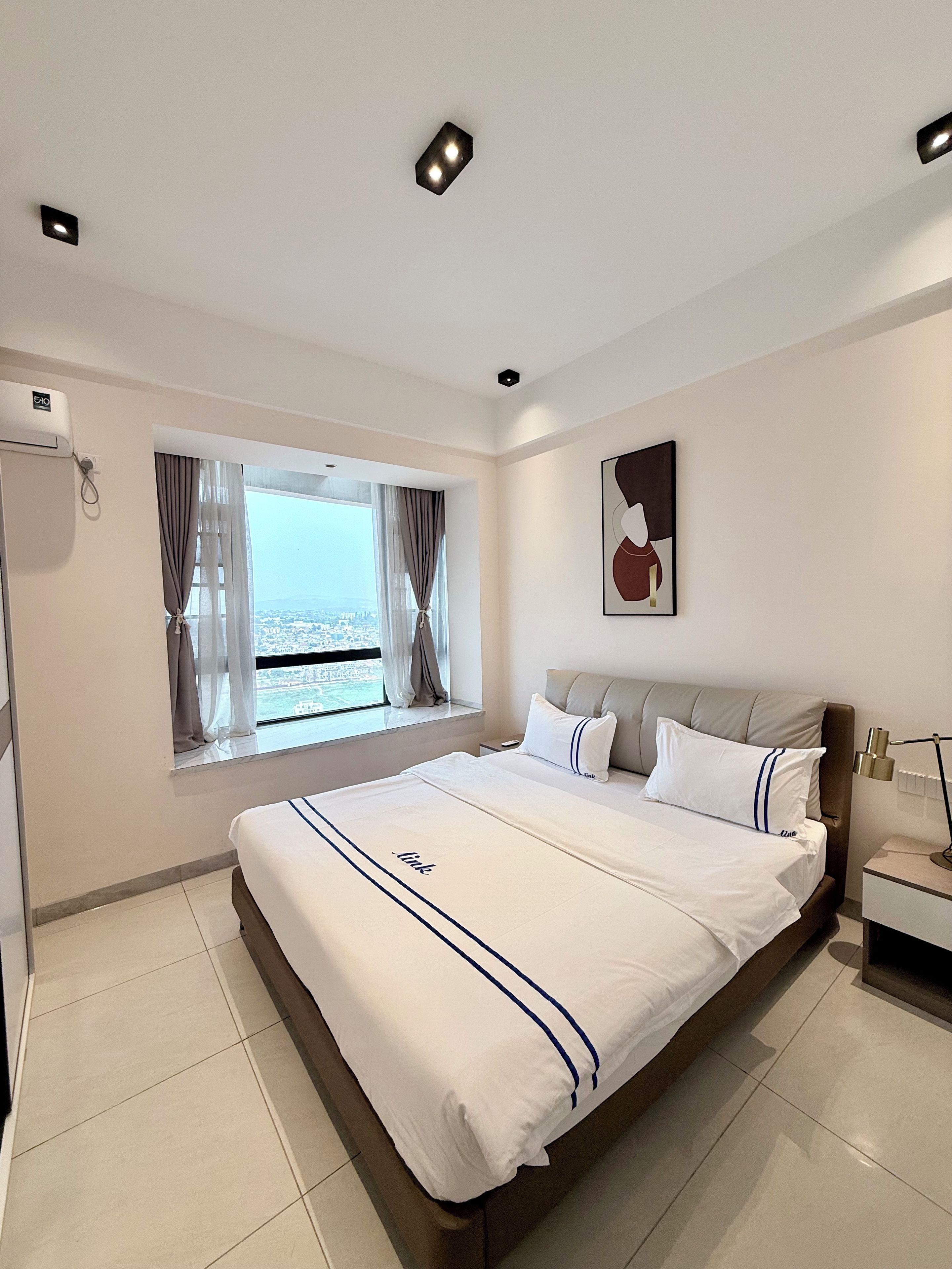 Une chambre d’hôtel moderne avec un grand lit, une fenêtre avec des rideaux, une table de chevet et une œuvre d’art accrochée au mur.