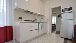 A modern kitchen with white cabinets, a stove, a microwave, and a refrigerator.