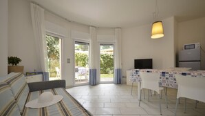 A modern living room with a sofa, a dining table with chairs, a TV, and a kitchen area with a refrigerator. - Sophistication and stylish vacation apartment (Bibione)