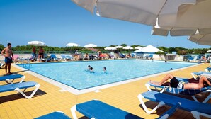 A swimming pool with sun loungers and umbrellas, surrounded by a tiled deck.