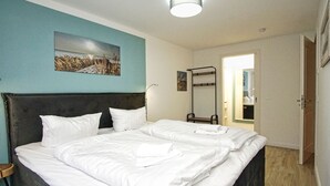 A double bed with white linens, a dark headboard, and a teal accent wall.