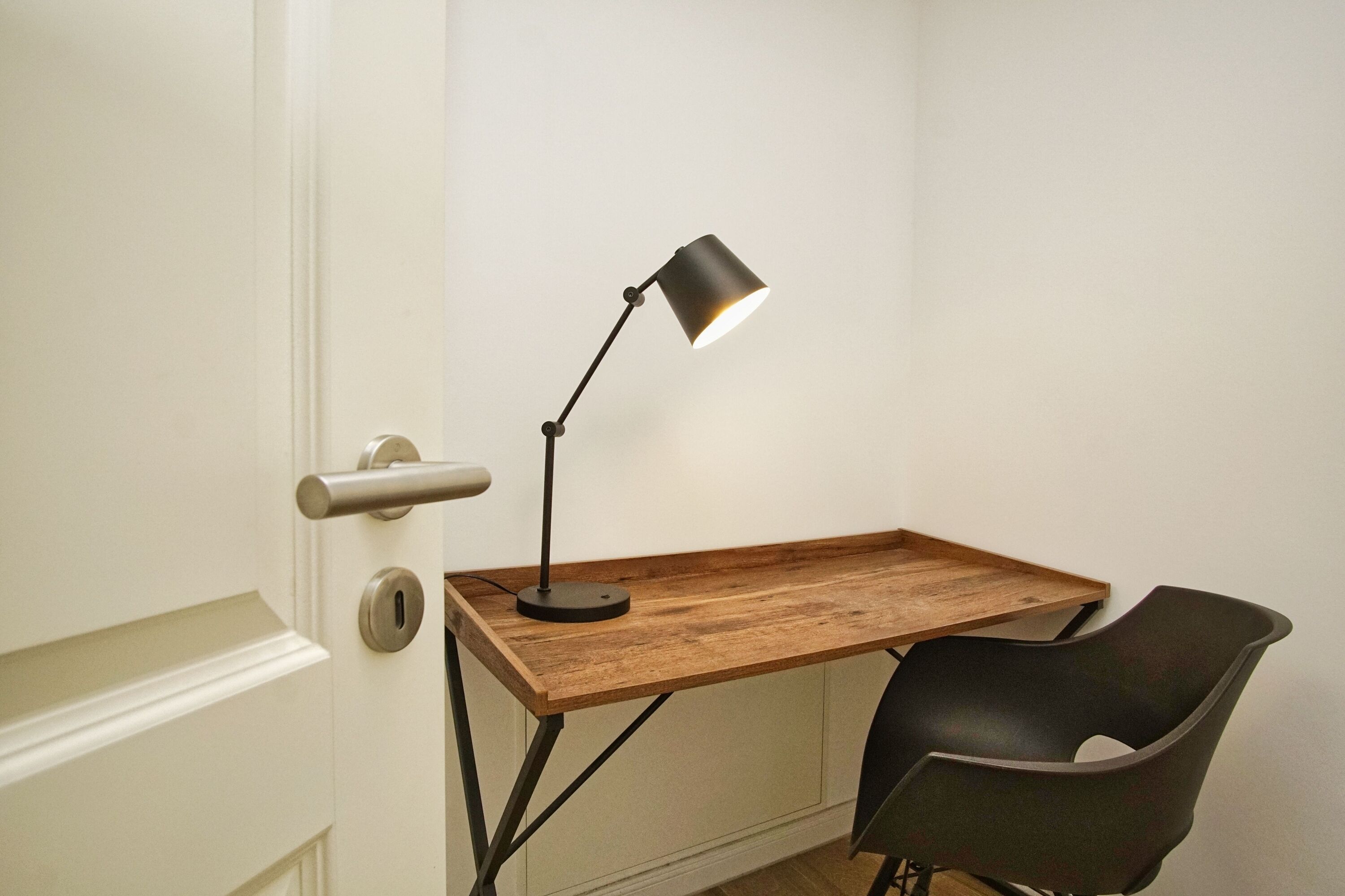 A desk with a lamp, a chair, and a door with a handle.