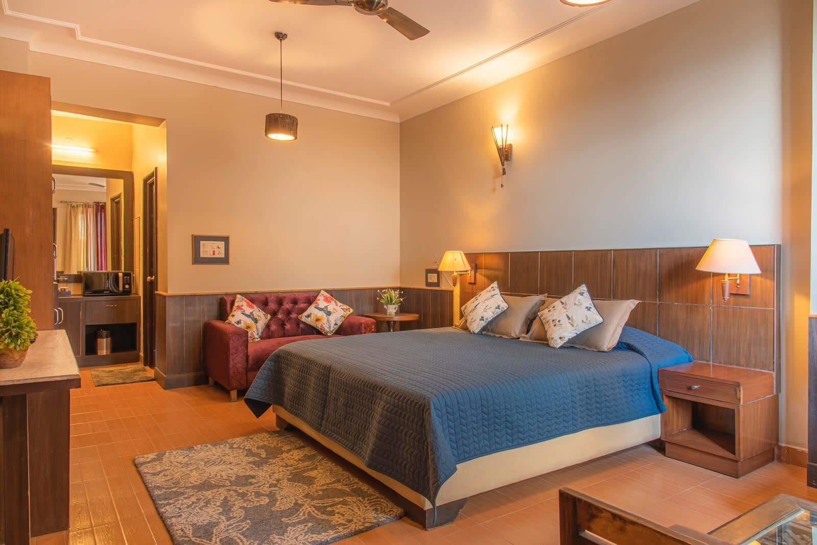 A bedroom with a bed, bedside tables, a nightstand, a red sofa, a ceiling fan, and a small plant.