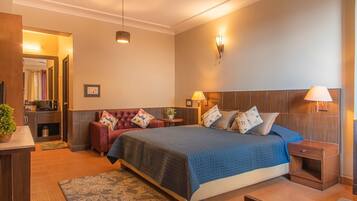 A bedroom with a bed, bedside tables, a nightstand, a red sofa, a ceiling fan, and a small plant.