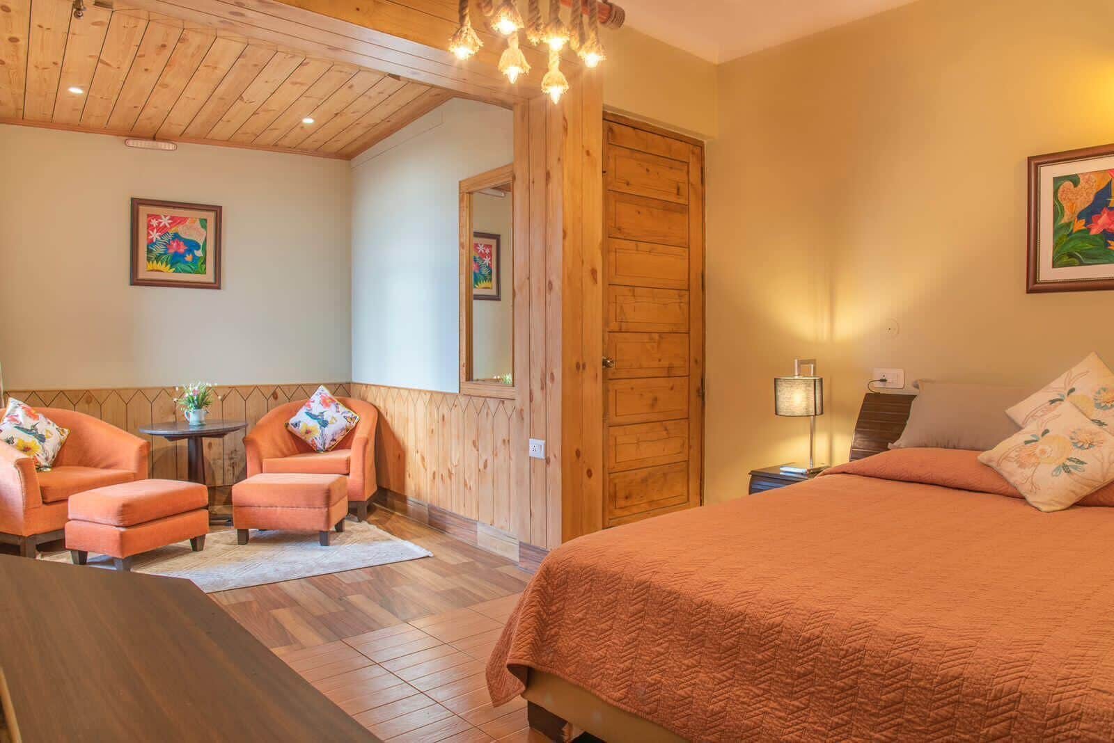 Um quarto acolhedor com uma cama, duas poltronas, uma mesinha e uma porta de madeira.