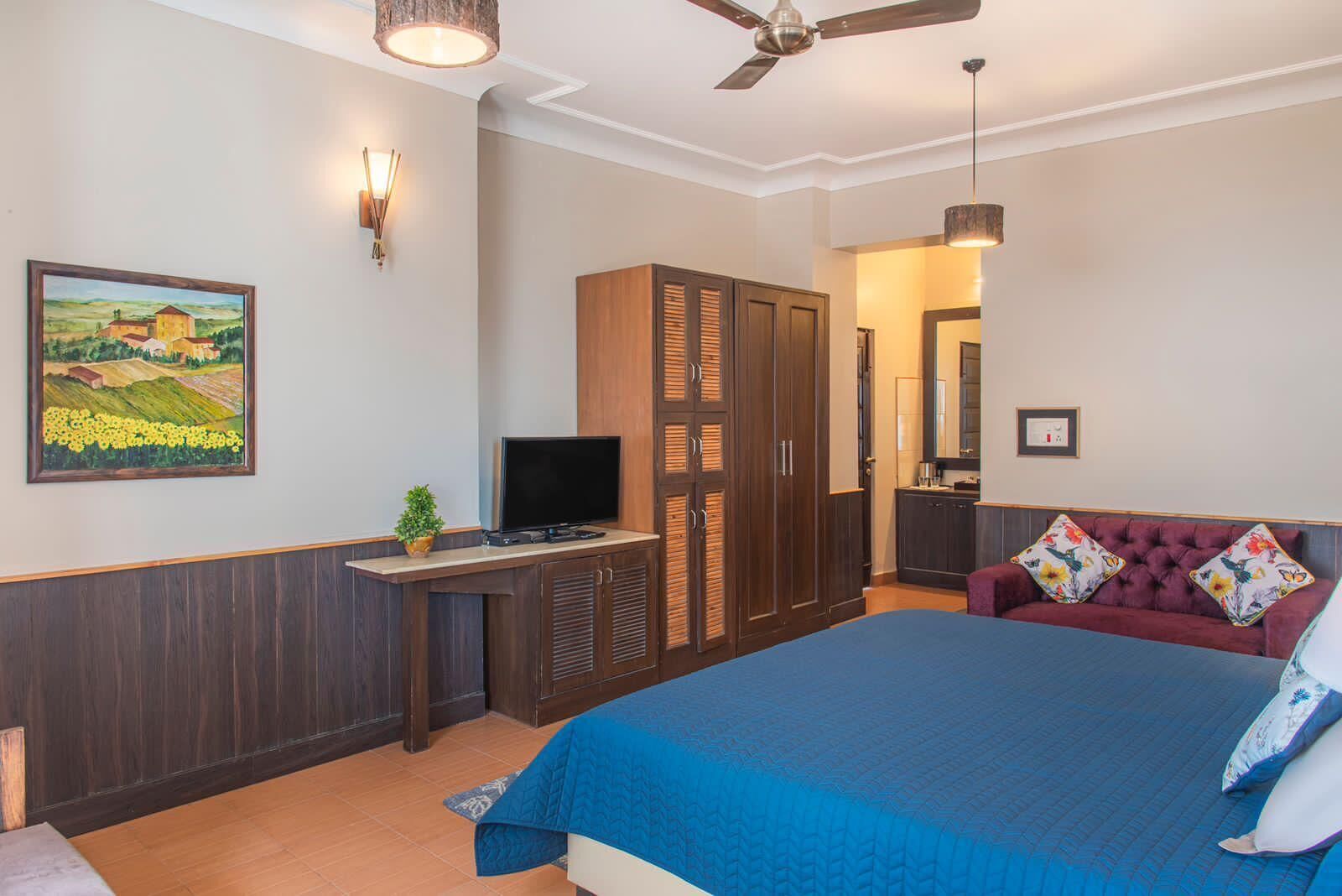 A bedroom with a bed, a desk with a TV, a wardrobe, and a painting on the wall.
