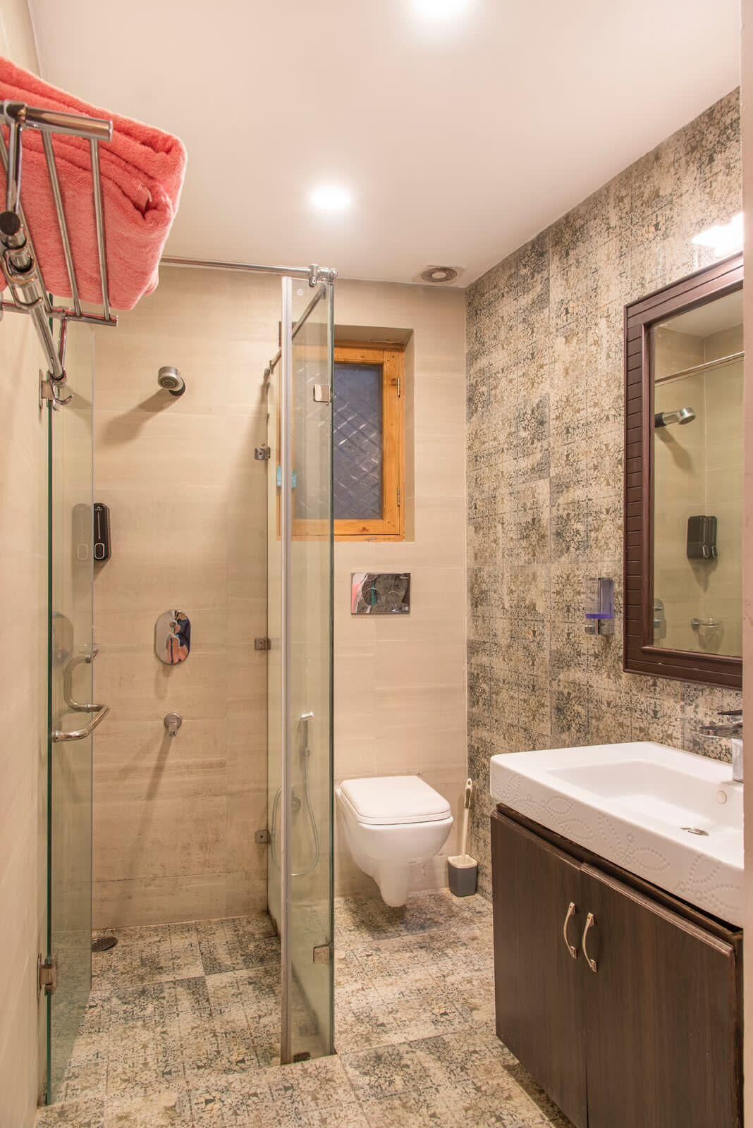 A bathroom with a glass shower enclosure, a toilet, a sink with a mirror, and a towel rack.