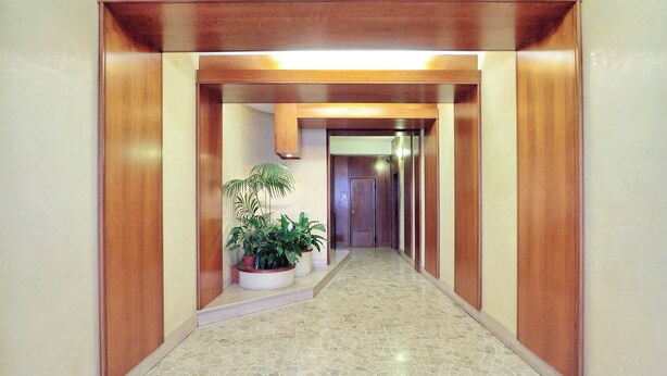 A hallway with a tiled floor, wooden paneling, and potted plants.